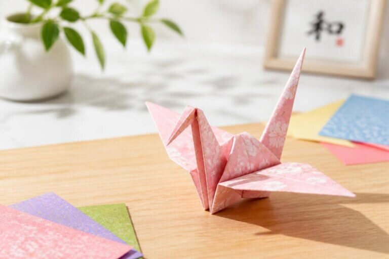 Un origami grue magnifiquement réalisé repose délicatement sur une table en bois clair, illuminé par la lumière du jour, avec des éléments flous en arrière-plan créant une atmosphère artistique et sereine.